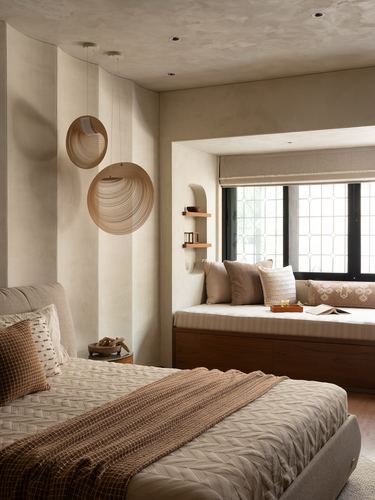 Bedroom with curved fluted plaster wall, disc pendant lights, and a window seat nook with storage