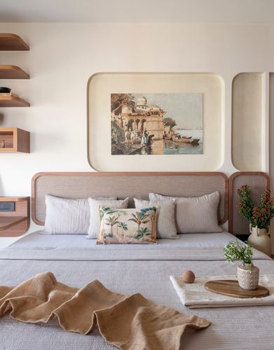 Bed with curved wood headboard beneath arched wall niches framing a painting, styled with linen throw and cushions