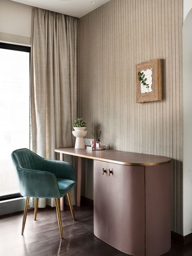 Blush pink curved writing desk with green velvet chair against ribbed taupe wallpaper