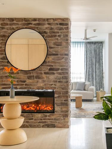 Stone-clad wall with round mirror and fireplace opens to a curtained living room beyond