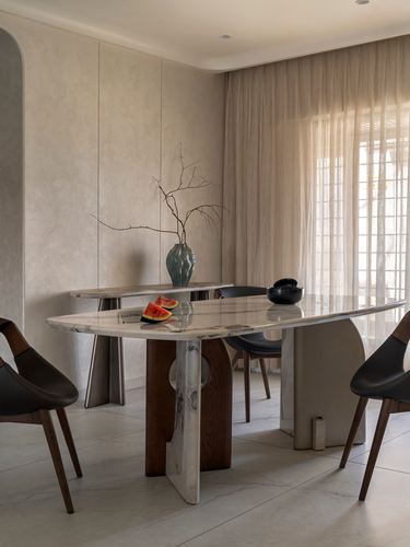 Dining room with sculptural marble table on wood legs, sheer curtains, and textured plaster walls
