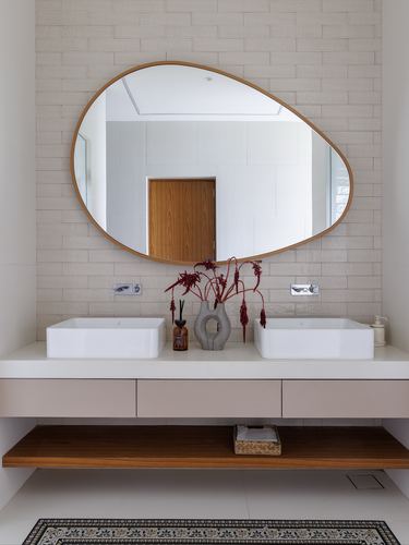 Double vanity bathroom with organic mirror, twin vessel sinks and wood open shelf below