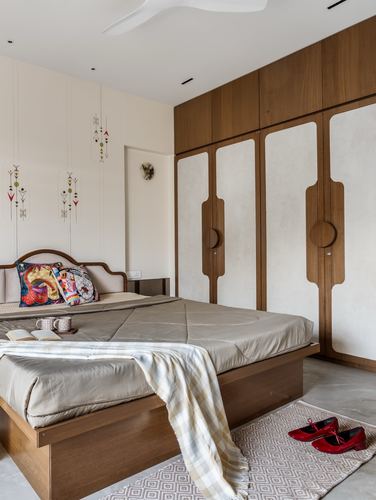 Bedroom with wooden wardrobe featuring round pulls, upholstered headboard, and patterned wall hangings