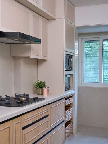Modern kitchen with beige upper cabinets, wood lower cabinets, gas hob, and window view of trees