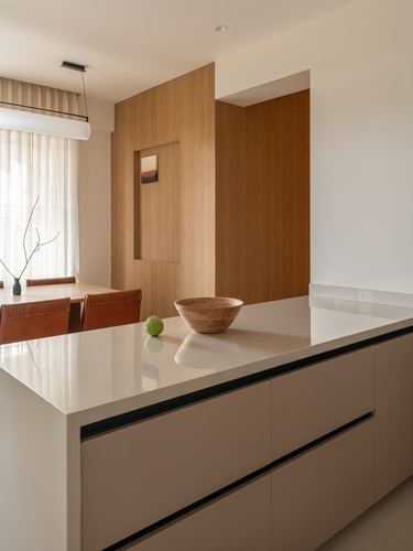 Kitchen island with stone countertop and wooden bowl, framed by a wood-paneled wall niche and dining nook beyond