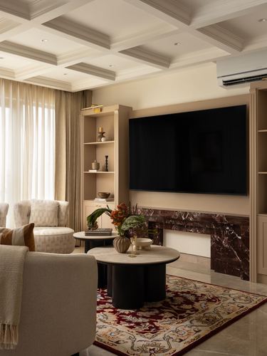 Beige living room with coffered ceiling, marble fireplace wall, layered coffee tables and patterned rug