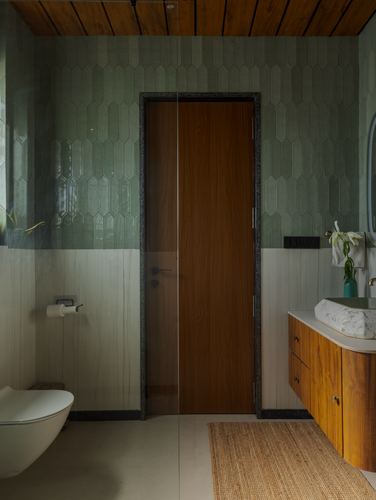 Bathroom with green scalloped tile, wooden door, marble vessel sink and jute rug