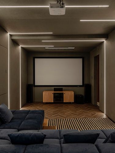 Home theater room with concrete walls, linear LED lighting, chevron wood floor, and blue sectional sofa