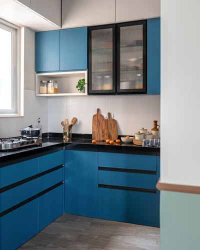 L-shaped modern kitchen with teal blue cabinets, black countertop, and fluted glass upper cabinet