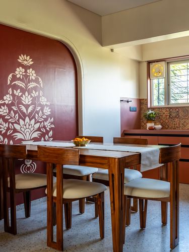 Dining area with wooden table, cane-less chairs, and maroon curved wall with white floral mural