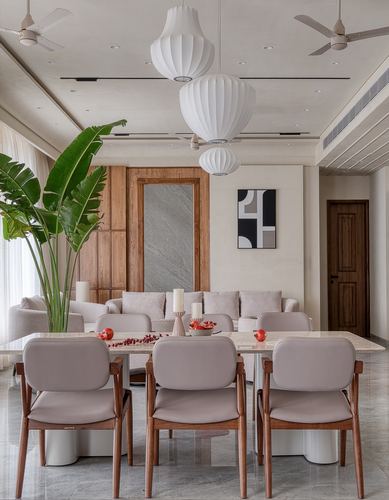 Dining area with marble table, cane-backed chairs, layered white pendant lights and a large plant