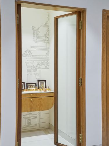 Open glass and wood door revealing a small pooja alcove with mural and shelf