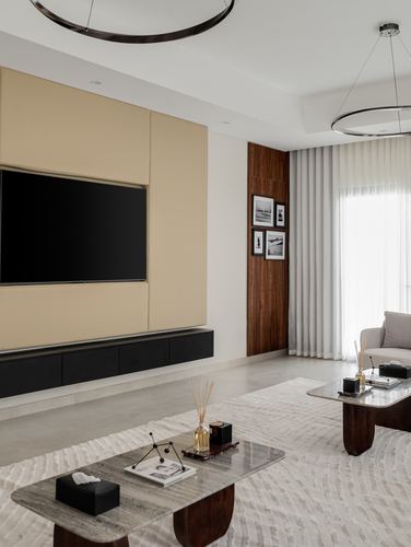 Living room with beige panelled tv wall, walnut accent, layered marble coffee tables and sheer curtained window