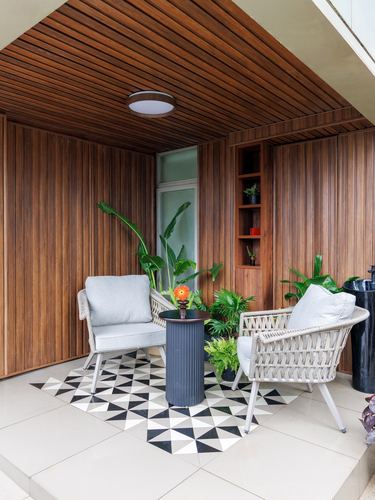 Wood-slatted balcony seating nook with woven chairs and black-and-white geometric tile floor