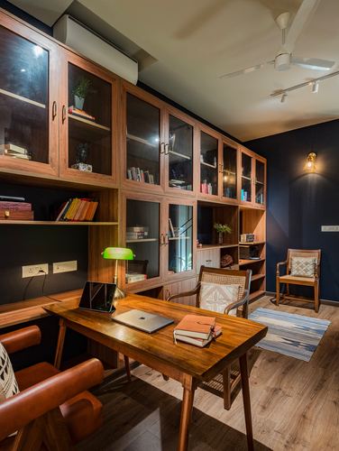 Wooden home study with cane chairs, floor-to-ceiling bookshelf, desk lamp, and navy accent wall