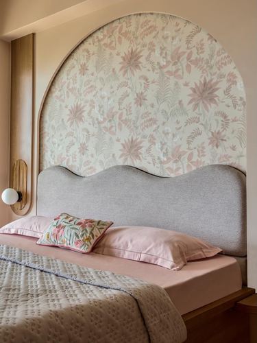 Bedroom with arched floral wallpaper niche and wavy grey upholstered headboard, pink bedding.