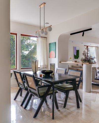 Dining room with black cane chairs around wood table, arched opening to living room, tall windows