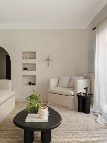 Minimalist beige living room with arched niche shelving, linen sofas, and black round tables