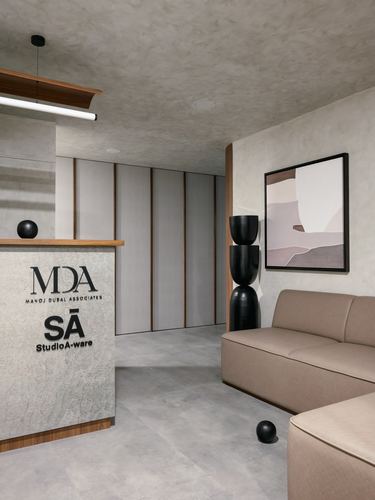 Reception area with concrete walls, wood-trimmed paneling, a taupe sofa, and abstract wall art.