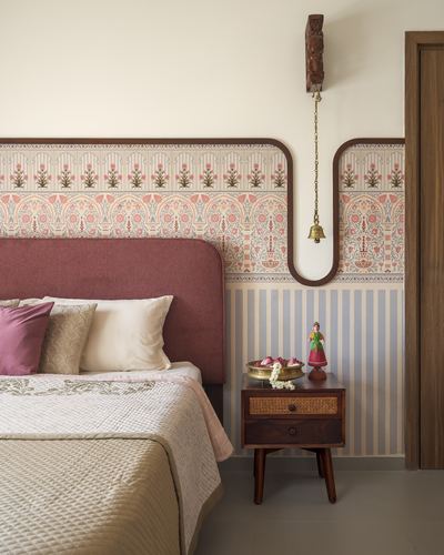 Bedroom with rose upholstered headboard, patterned wallpaper border, and hanging brass bell over wooden bedside table