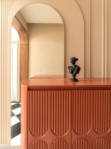 Terracotta fluted cabinet with black bust sculpture beneath an arched mirror in a beige foyer