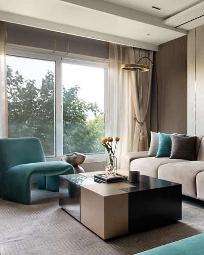 Living room with teal velvet armchair, sofa, and layered coffee table beside large window