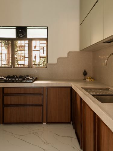 L-shaped kitchen with walnut cabinetry, curved beige backsplash and stone counters lit by a window