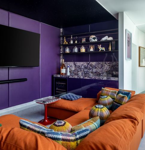 Media lounge with purple lacquered bar wall, starry black ceiling, and orange sectional sofa with knit pillows