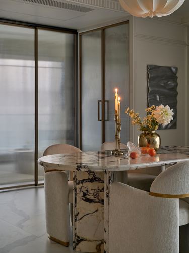 Round marble dining table with brass candlestick and flowers, upholstered chairs, pendant light above