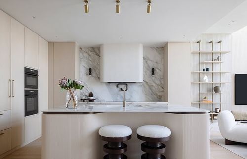 Cream kitchen with marble backsplash, curved fluted island, and dark wood stools under brass pendant lights