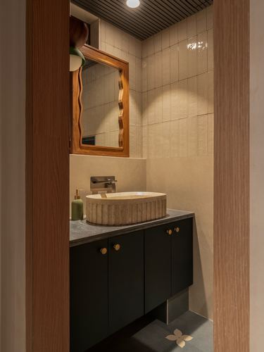 Bathroom vignette through wooden doorway with fluted stone sink, wavy mirror, and black vanity.