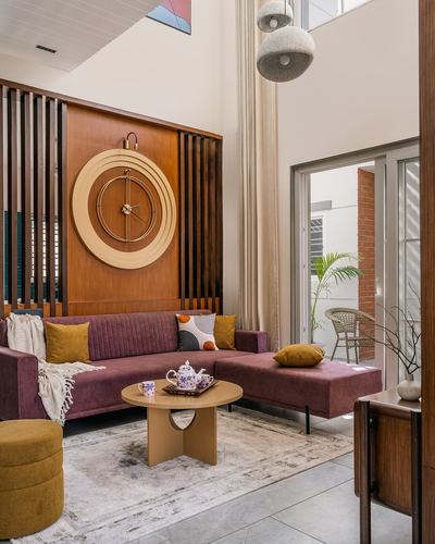 Living room with maroon sectional sofa, mustard cushions, and large round wooden clock on slatted wall