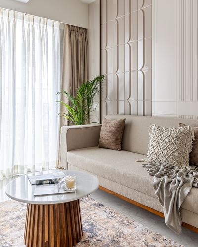 Beige sofa with textured cushions beside round marble-top coffee table and sheer curtains