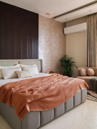Bedroom with channel-tufted grey bed, orange throw, fluted wood accent wall and textured plaster