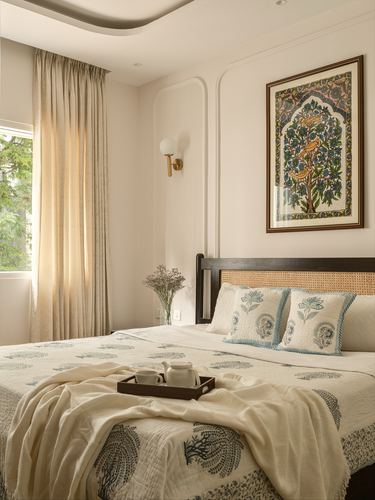 Bedroom with cane headboard bed, block-print linens, framed art and curved plaster wall niche
