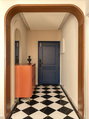 Foyer passage with terracotta cabinet, checkerboard marble floor, and blue panelled door at end