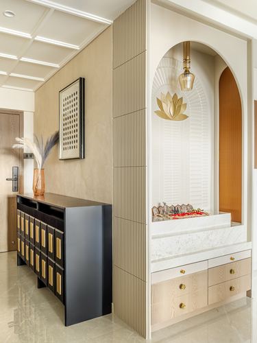 Arched pooja niche with fluted white plaster, lotus motif, marble counter, and wooden storage beside a corridor console