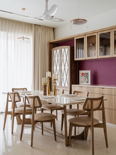 Dining room with cane chairs, wood table, and maroon accent wall behind glass-front cabinets