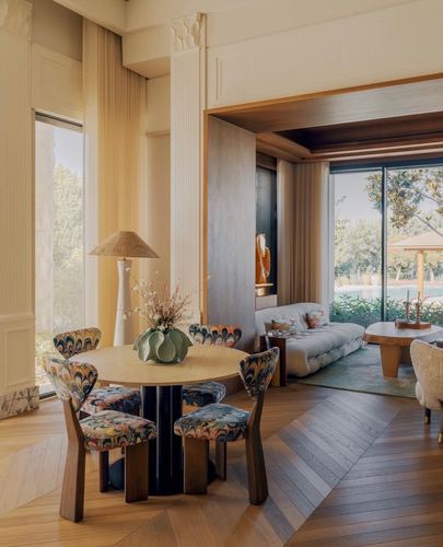 Round dining table with patterned chairs framed by fluted columns, opening to living room and garden
