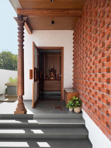 Entrance porch with carved wooden pillar, brick wall, and open door revealing a deity niche