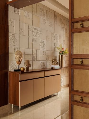 Foyer with textured leaf-patterned stone wall behind a terracotta console and decorative brass objects