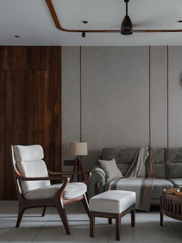 Living room corner with wooden armchair, ottoman, tripod lamp and grey sofa against panelled walls