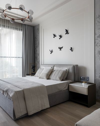 Grey upholstered bed beneath flying bird wall decor, wood floor, sheer curtained window