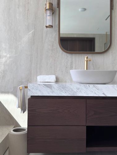 Marble-topped vanity with vessel sink, brass faucet, and dark wood drawers below arched mirror