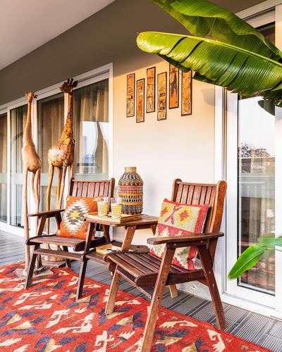 Balcony seating with wooden chairs, kilim cushions, giraffe sculptures and a red tribal rug