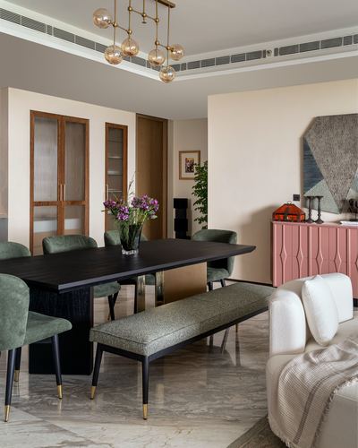 Dining room with dark wood table, green velvet chairs, bench, and pink sideboard on marble floor