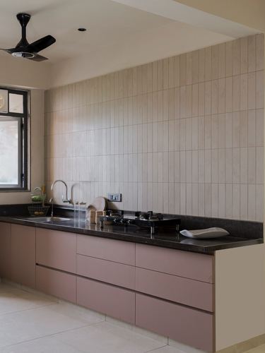 Kitchen counter with pink cabinetry, dark stone countertop, and vertical ribbed tile backsplash