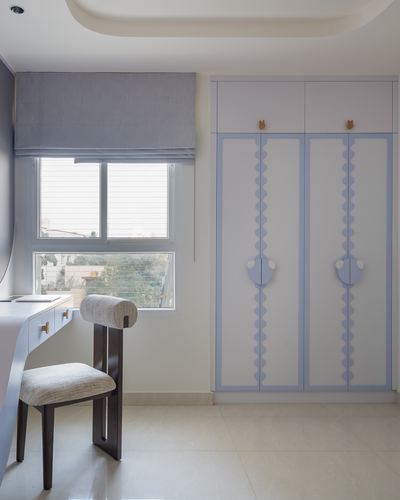 Child's bedroom with scalloped blue-trimmed wardrobe, desk, window and grey roman blind