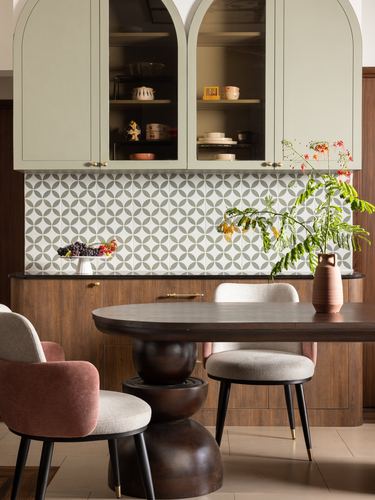 Dining area with arched sage cabinets, patterned tile backsplash, and sculptural wood table