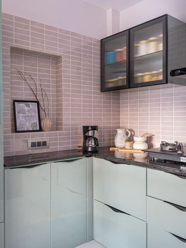 L-shaped kitchen corner with mauve tile backsplash, sage green cabinetry, and a black-framed glass wall cabinet